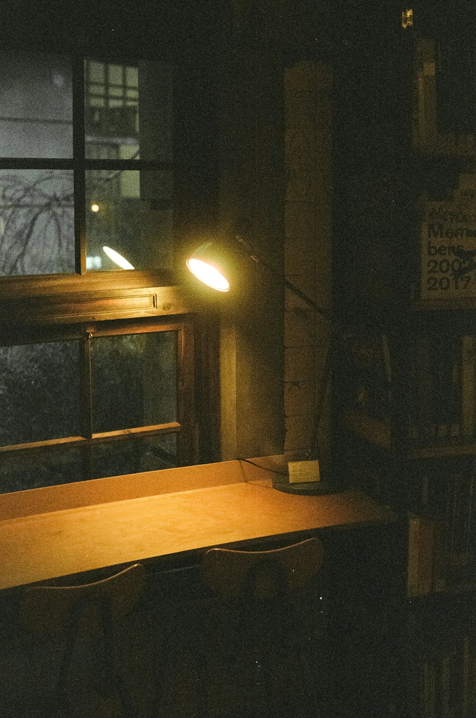 Ein leerer Schreibtisch aus Holz steht nachts am Fenster.